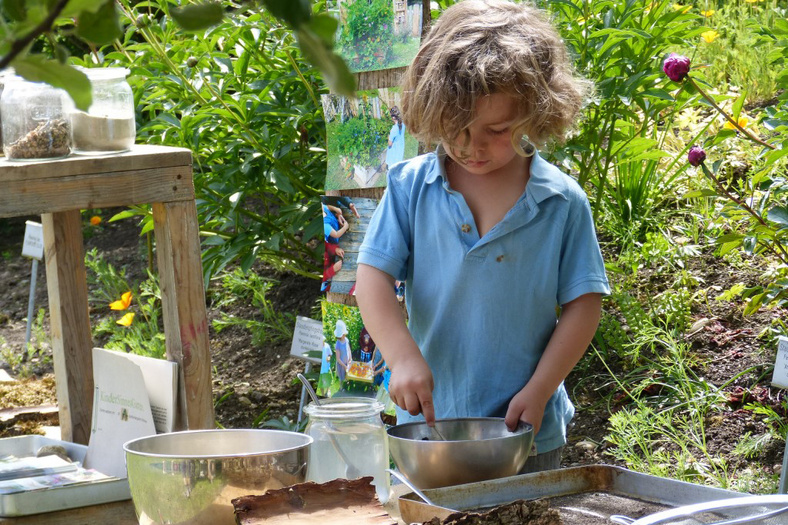 Nahaufnahme eines Kindes im Kindersinnesgarten des Waldorfkindergartens in Wahlwies, wie es Samenkugeln herstellt