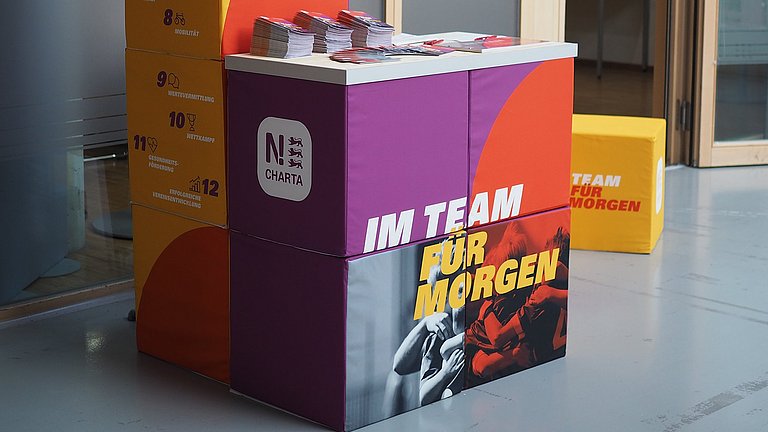 Auf einer Theke aus Stoffwürfel mit der Aufschrift "Im Team für morgen" liegt Informationsmaterial zur N-Charta Sport.