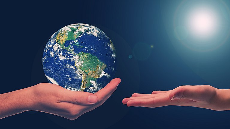 Eine Hand hält schützend die Erdkugel, ihr gegenüber ist eine weiter Hand bereit die Erde in Empfang zu nehmen.