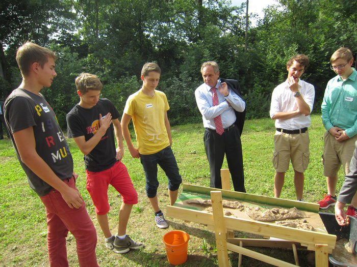Innenminister Reinhold Gall und fünf Schüler auf der Wiese neben einem Holzgestell. 
