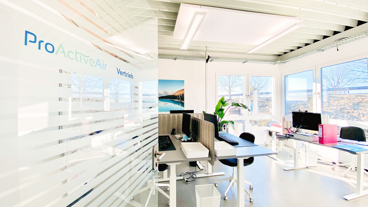 Ausschnitt eines Büros der ProActiveAir GmbH mit Schreibtischen, Stühlen und großen Fenstern.
