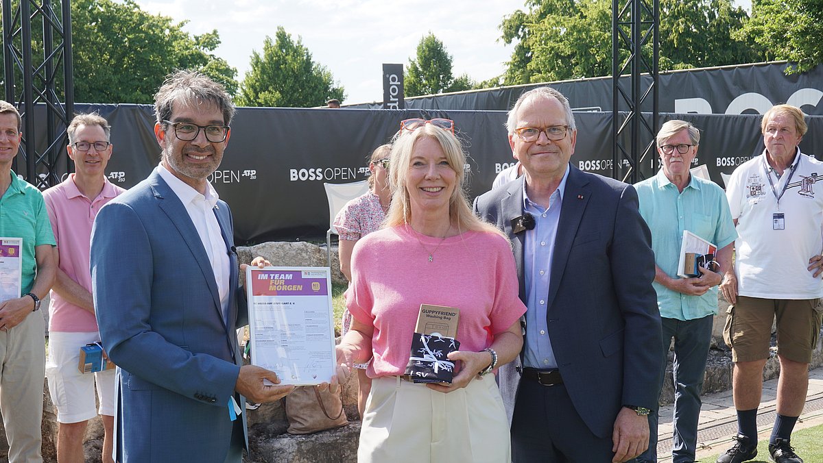 Staatssekretär Andre Baumann stehet neben einer Mitgliederin des TC Weiß-Rot und überreicht die N!-Charta Sport Urkunde.