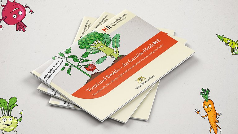 Drei Malbücher Tomti und Brokki, die Gemüse-Helden, liegen übereinander auf einer Arbeitsfläche. Von allen vier Ecken schauen gezeichnete Gemüsefiguren ins Bild.