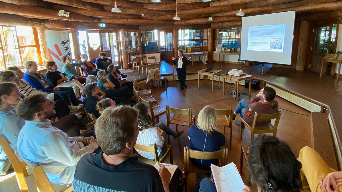 Teilnehmende einer Veranstaltung sitzen im Kreis und lauschen einer Präsentation.