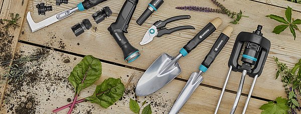 Eine Auswahl verschiedener Gartenhandgeräte liegen aufgereit auf einem Brett.