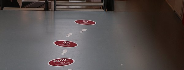 Bodenaufkleber mit Fußstapfen und Info-Kreisen zum Thema Nachhaltigkeit.