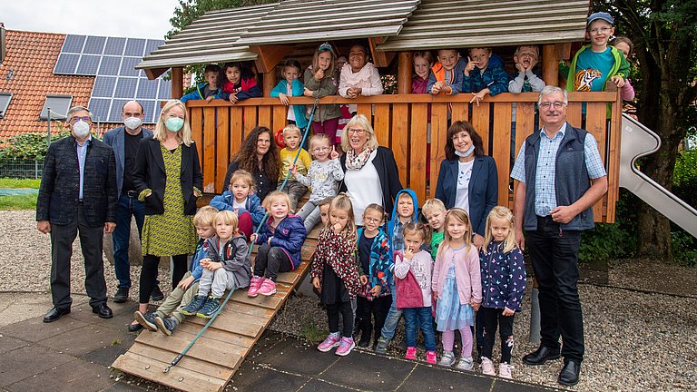 Eine Gruppe von Erwachsenen und Kindern im Kindergartenalter, die auf vor und auf einer Hütte stehen und in die Kamera blicken.