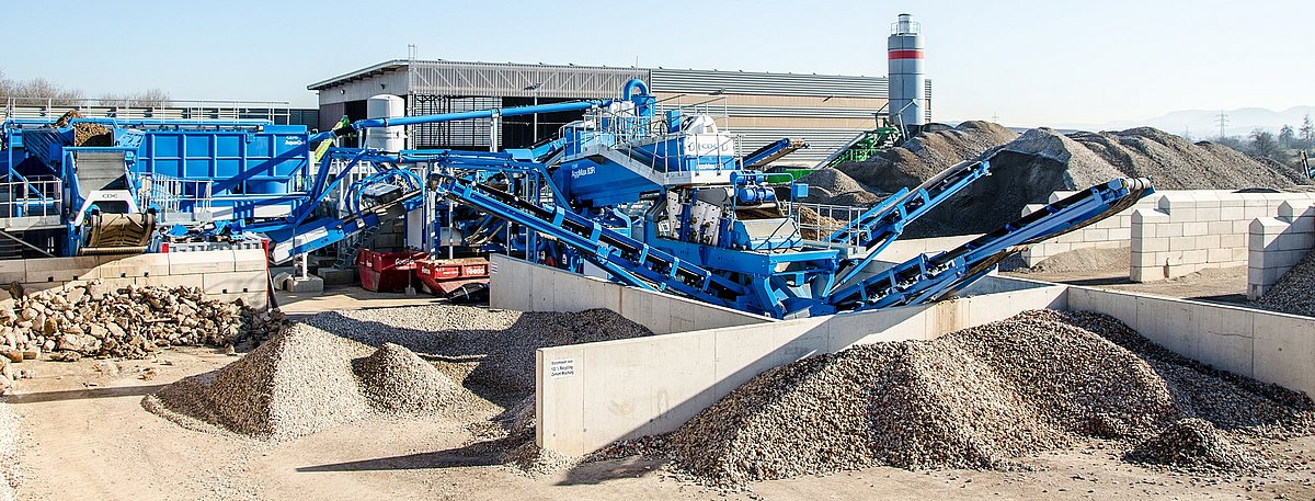 Eine blaue, stählerne Anlage, umgeben von Baustoffen, unter einem klaren, blauen Himmel.