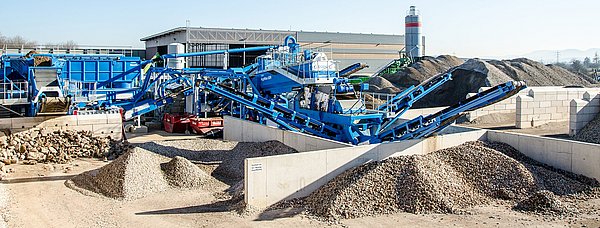 Eine blaue, stählerne Anlage, umgeben von Baustoffen, unter einem klaren, blauen Himmel.