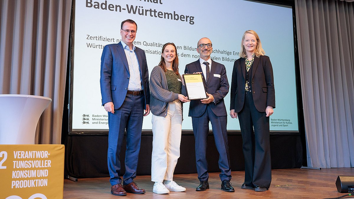 Umweltministerin Thekla Walker MdL und Kultusstaatssekretär Volker Schebesta MdL stehen zusammen mit einer Frau und einem Mann auf einer Bühne. Sie lächeln alle in die Kamera, die Umweltministerin und Vertreter des Naturparks Stromberg-Heuchelberg halten ein eingerahmtes BNE-Zertifikat.