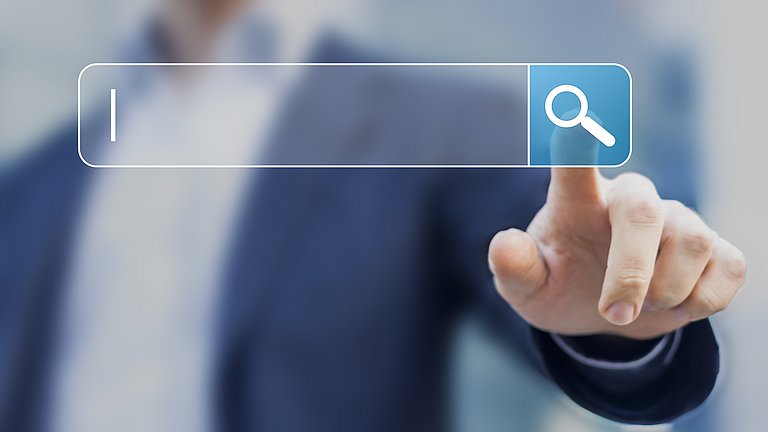 Im Hintergrund sieht man den verschwommenen Oberkörper einer Person. Im Vordergrund wurde eine Suchleiste eingeblendet. Die Person klickt dabei auf eine Lupe und startet somit eine digitale Suche.