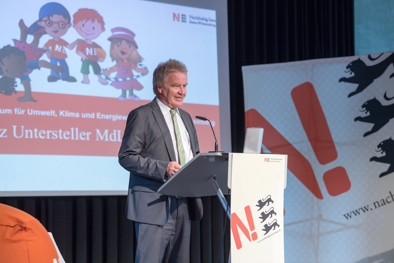 Herr Minister Franz Untersteller steht vor einem Rednerpult und hält eine Rede