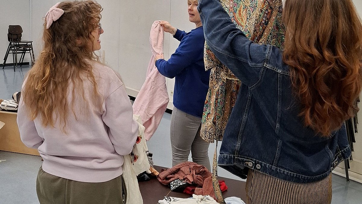 Frauen suchen nach passenden Kleidungsstücken, welche ausgebreitet auf einem Tisch liegen.