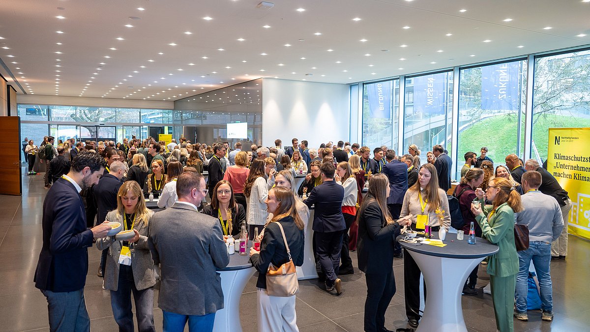 Besucherinnen und Besucher des Kongresses stehen im Foyer an Stehtischen und unterhalten sich.
