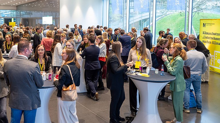 Besucherinnen und Besucher des Kongresses stehen im Foyer an Stehtischen und unterhalten sich.