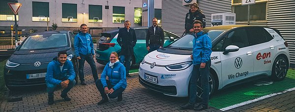 Mitarbeiter des Autohaus Haitzler bei einem Besuch des „Marathonfahrers“ Rainer Zietlow im Autohaus Haitzler. Im Hintergrund sind drei PKW zu sehen, darunter ein E-Auto, das gerade an der öffentlichen Ladesäule des Autohauses geladen wird.