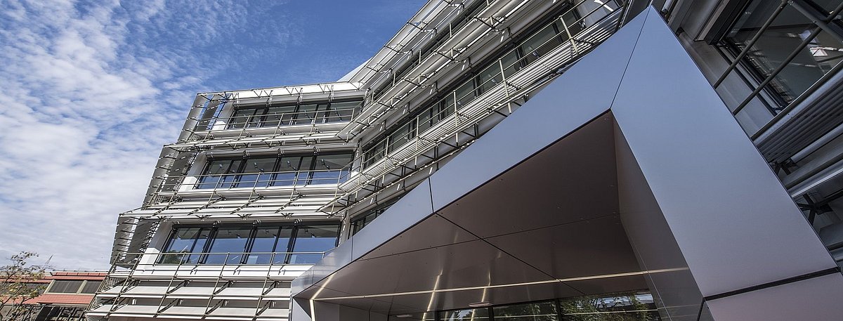Auf dem Bild ist das Gebäude der Stadtwerke Karlsruhe zu sehen. Die Sonne spiegelt sich in der grau-schwarzen Fassade mit den großen Fensterscheiben.