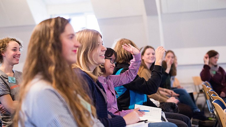 Nahaufnahme von mehreren Schülern, die einem Vortrag zuhören und sich zu Wort melden.