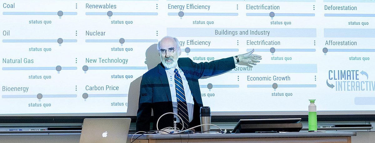 Ein Referent steht vor einer Präsentationsfläche und spricht zum Publikum.