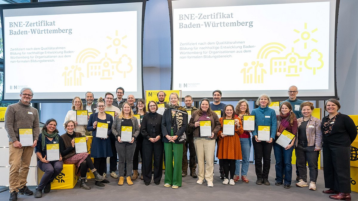 Alle Personen, die eine BNE-Zertifizierung erhalten haben, stehen gemeinsam mit ihrer Urkunde in den Händen mit Umweltministerin Thekla Walker und Kultusstaatssekretärin Sandra Boser auf der Bühne.