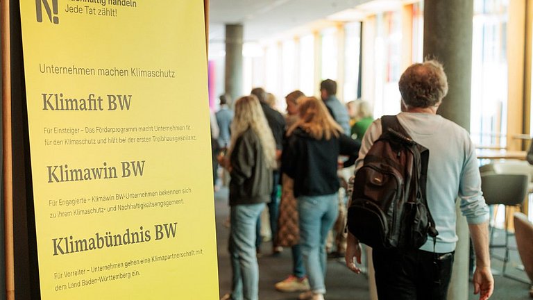 Menschen laufen in einem Foyer an einem Banner der Nachhaltigkeitsstrategie vorbei.