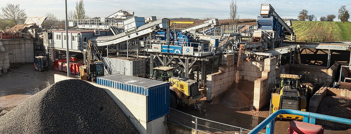 Eine blaugraue, stählerne Anlage, umgeben von Baustoffen, unter einem klaren, blauen Himmel.