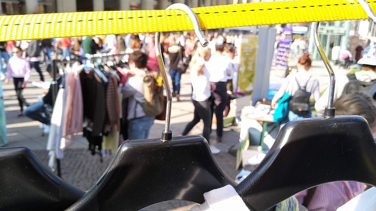 Nahaufnahme eines Kleiderbügels mit Flohmarkt im Hintergrund.