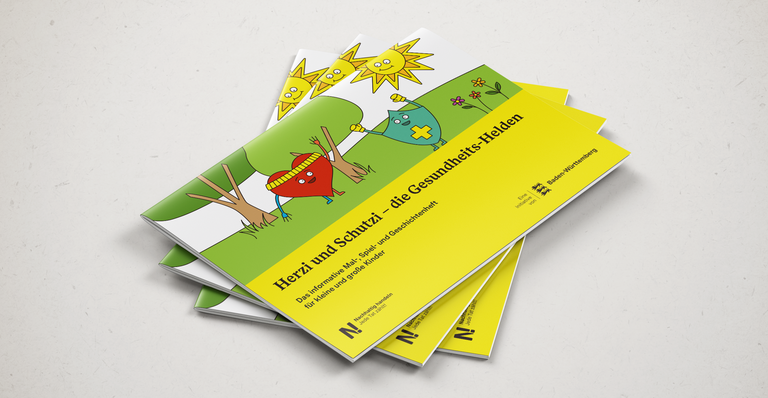Drei Malbücher, Herzi und Schutzi, die Gesundheitshelden, liegen übereinander auf einer grauen Fläche.