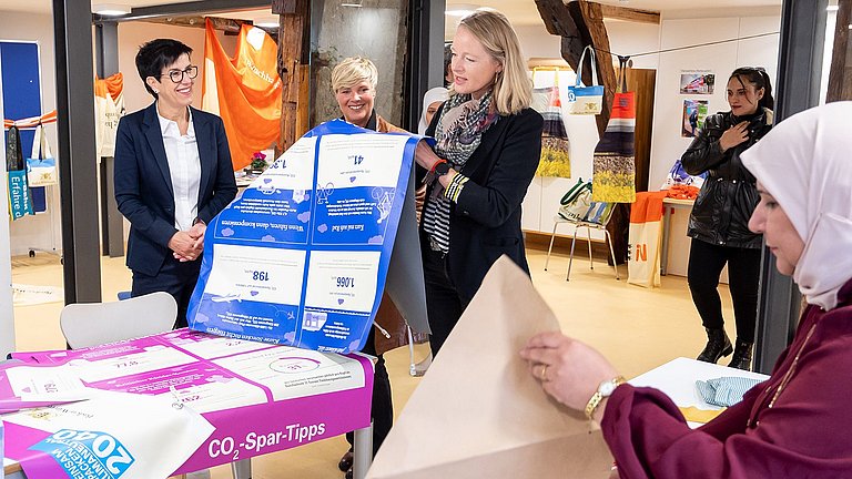 Umweltministerin Thekla Walker, Oberbürgermeisterin von Metzingen Carmen Haberstroh, Landtagsabgeordnete Cindy Holmberg und weitere Besucher des Nähcafes Metzingen begutachten aussortierte Banner der Nachhaltigkeitsstrategie Baden-Württemberg.