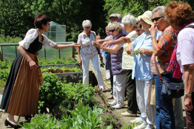 Bernadette Schrödel steht in einem Gemüsegarten und zeigt diesen neugierigen Besuchern
