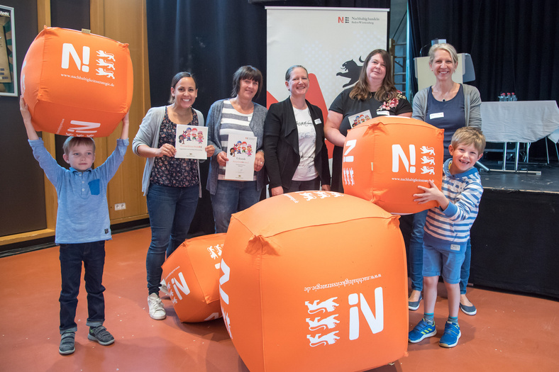 Fünf Frauen posieren für ein Foto und zwei Kinder spielen mit den orangenen Nachhaltigkeitsstrategier-bällen