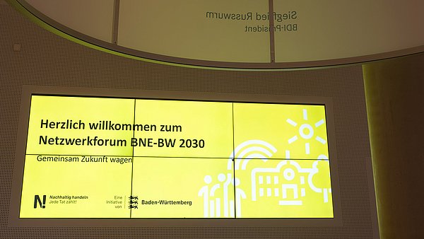 Foyer des Look21 in Stuttgart, Besucherinnen und Besucher werden mit einer Projektion auf der „Herzlich willkommen zum Netzwerkforum BNE-BW 2030" begrüßt.