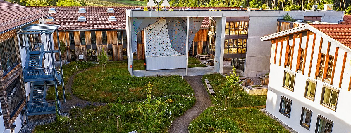 Außenansicht des VAUDE Gebäudes mit Gartenbereich und Kletterwand.