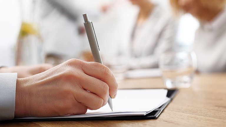 Eine Person schreibt mit einem Kugelschreiber Notizen auf einem Block.