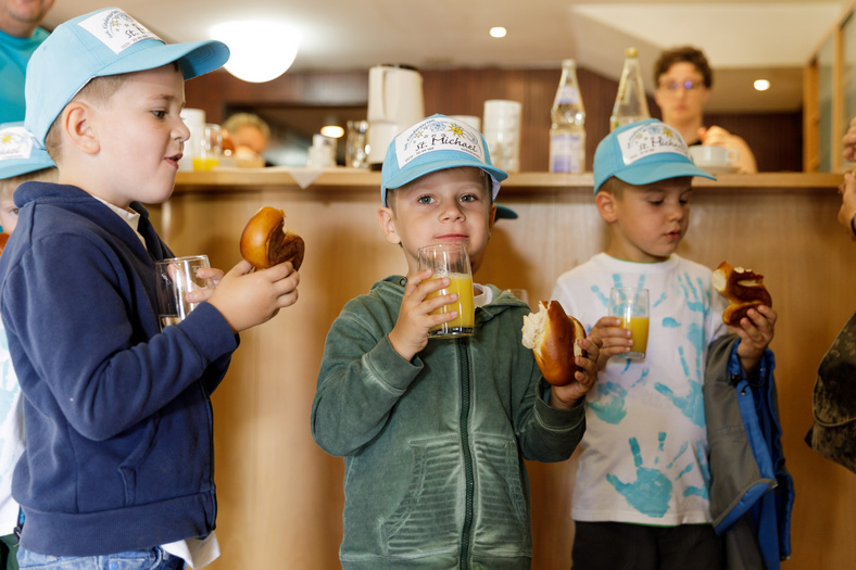 Drei Jungs mit gleicher blauer Kappe essen Brezeln und trinken Orangensaft