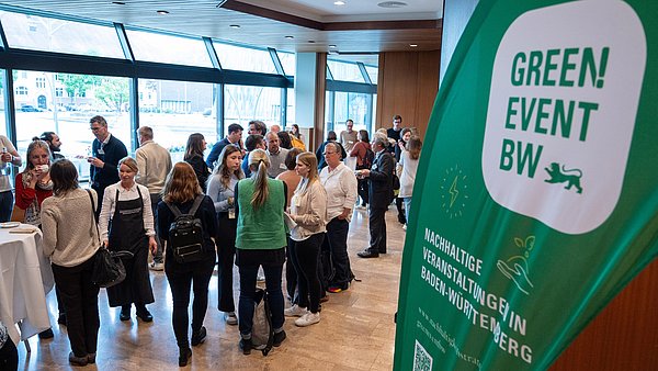 Teilnehmende des KLIMAWIN-Workshops stehen im Foyer, rechts ist die grüne Beachflag mit dem Green Event Siegel zu sehen.