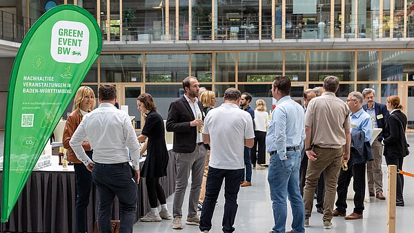 Foyer des SpOrt Stuttgarts gefüllt mit Teilnehmenden und einer Green Event Beachflag an der Seite.