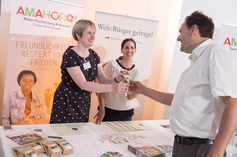Zwei Frauen hinter einem Infostand. Sie reichen einer Person etwas.