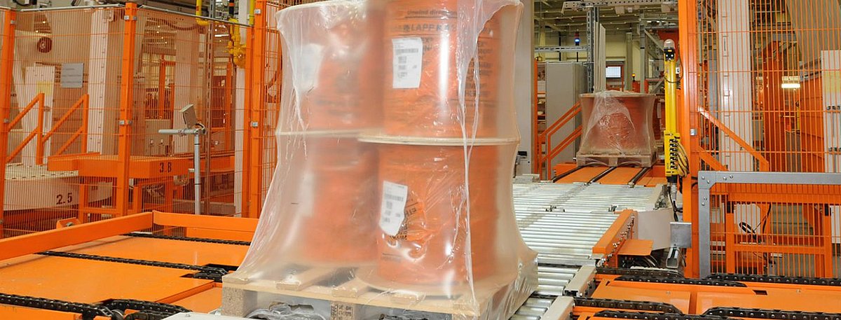 Eine Palette mit vier Kabeltrommeln sind von einer Sehrumpffolie umgeben. Sie verlassen gerade die Sehrumpfanlage.