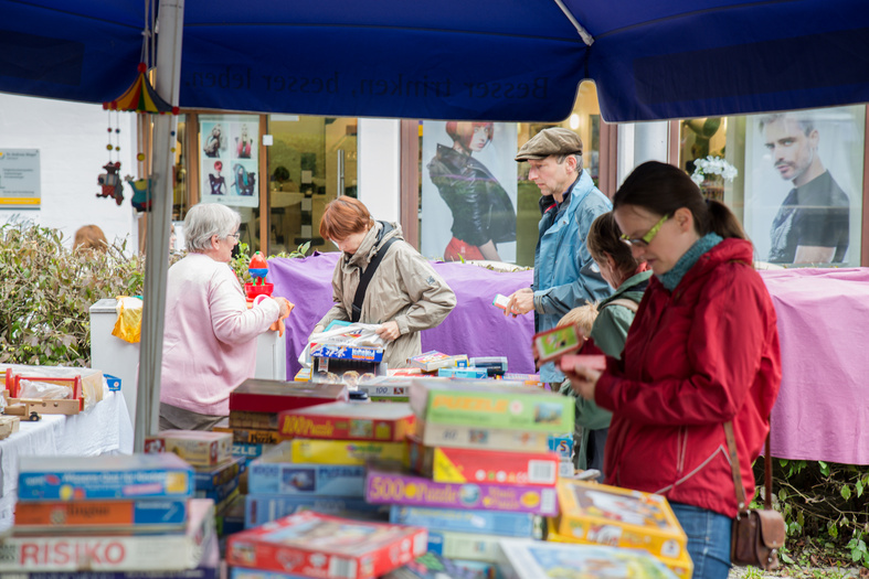 Flohmarkt. Ein Stand mit Brettspielen. Eine Frau schaut sich ein Spiel an.