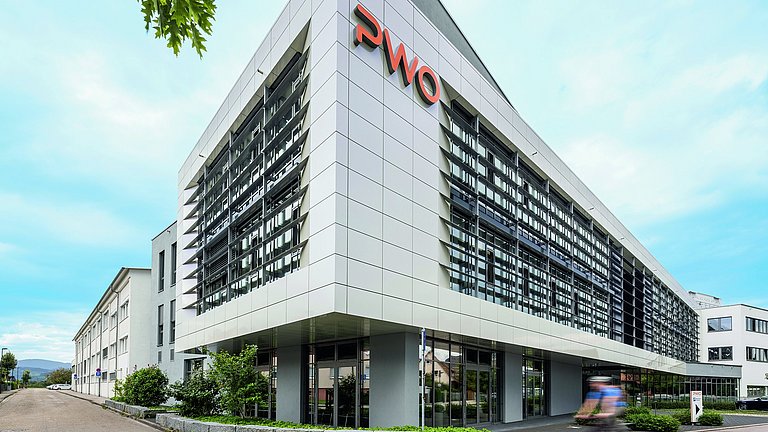 Weißes hohes Bürogebäude mit der orangefarbenen Aufschrift PWO.
