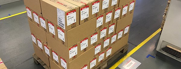 Eine Palette ist beladen mit vielen Karton, bei denen anstatt einer Strechfolie als Transportsicherung ein Klebeverfahren eingesetzt wird.