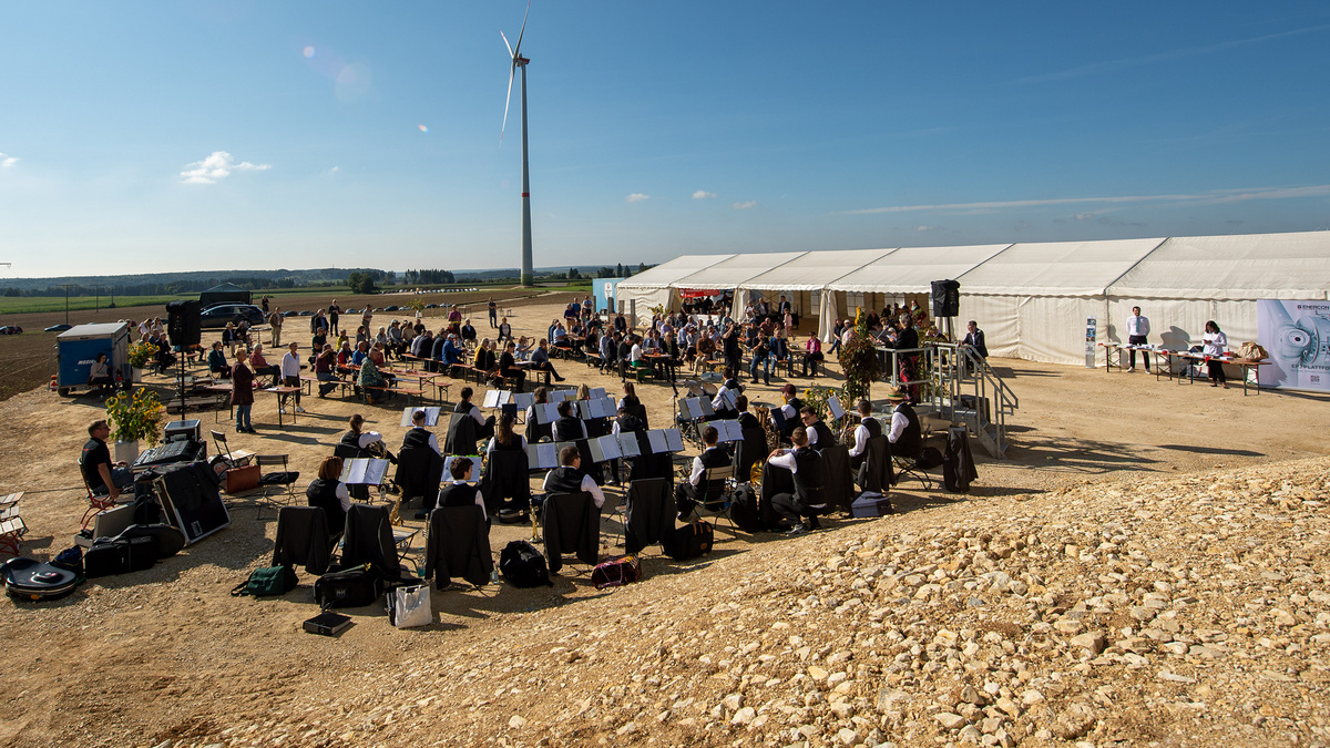 Auf einem freien Feld findet eine Veranstaltung mit Bläsermusikgruppe, Publikum und großem Zelt statt.