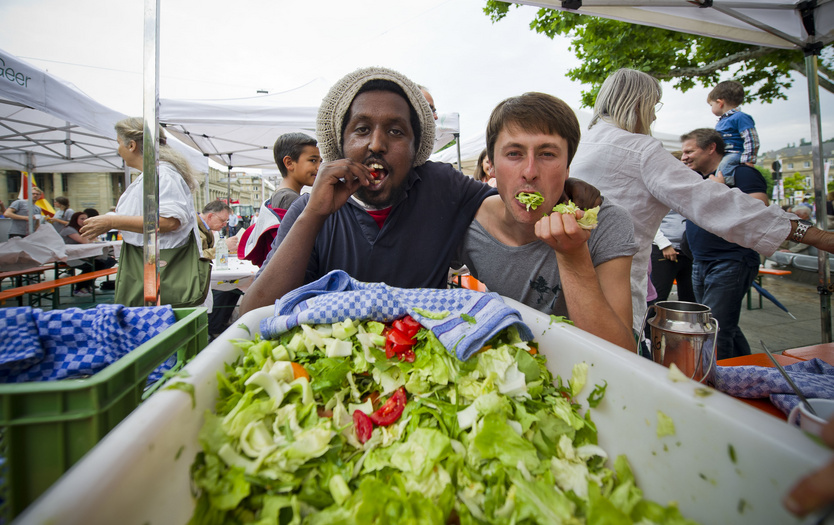 Nachhaltigkeitstage 2014 Zwei junge Männer Arm in Arm hinter einer Wanne mit Salat, essen Salatblätter und Tomate. Im Hintergrund Biergarnituren und Zelte.