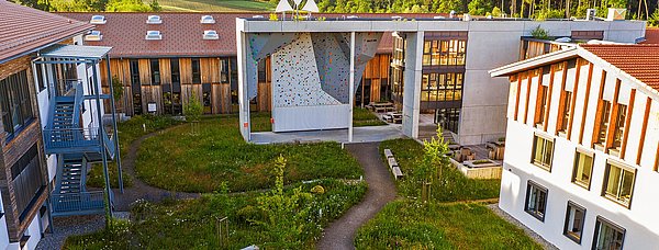 Außenansicht des VAUDE Gebäudes mit Gartenbereich und Kletterwand.