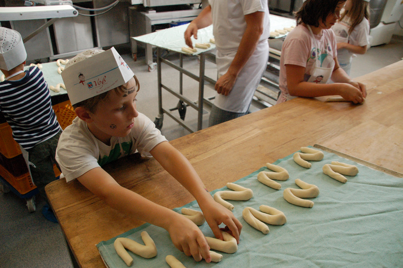 Nachhaltigkeitstage 2014 Ein Kind in der Backstube legt Teiglinge in der Form eines N auf ein Backblech.