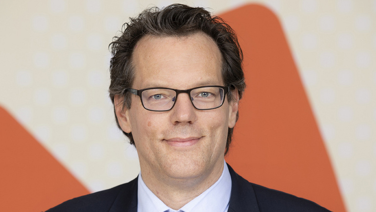 Prof. Dr.-Ing. Jörn Birkmann Prof. Dr.-Ing. Jörn Birkmann steht vor einem Plakat. Auf diesem ist ein orangenes N zu sehen.