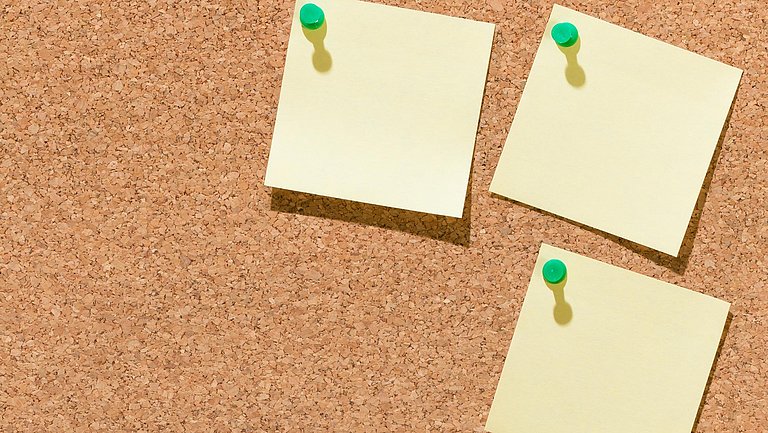 Eine Korkwand mit drei angepinnten, gelben Notizblättern. 