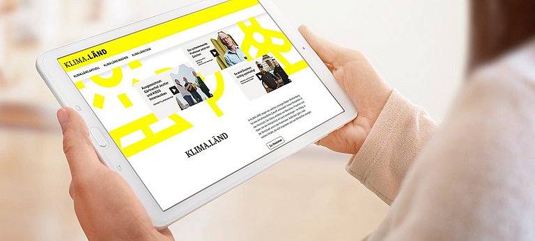 Frau hält Tablet in der Hand auf dem die Startseite klimalaendtage-Website zu sehen ist.