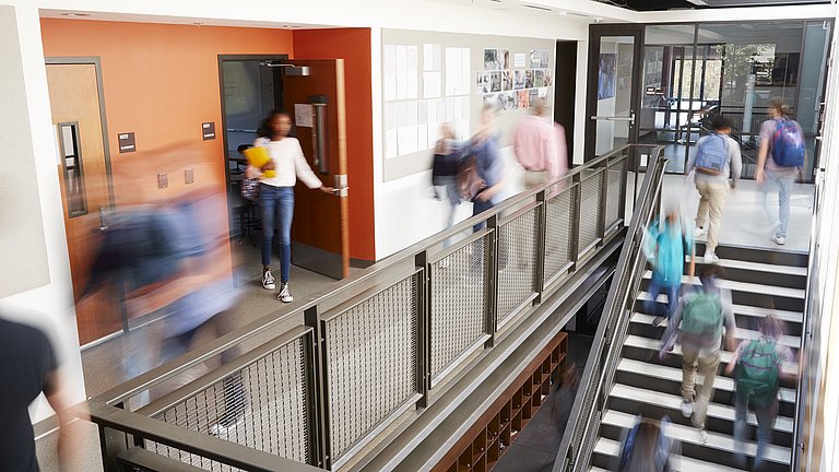 In einem Treppenhaus einer Schule sind verschiedene Schülerinnen und Schüler unterwegs.